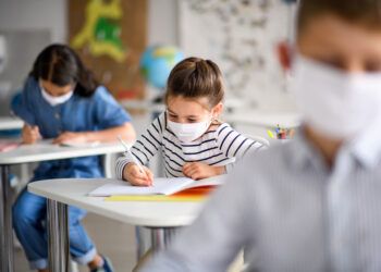 Small children with face mask back at school after covid-19 quarantine and lockdown, writing.