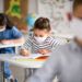 Small children with face mask back at school after covid-19 quarantine and lockdown, writing.
